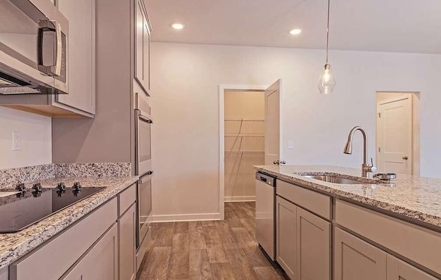 kitchen featuring sink, wood-type flooring, hanging light fixtures, stainless steel appliances, and light stone countertops