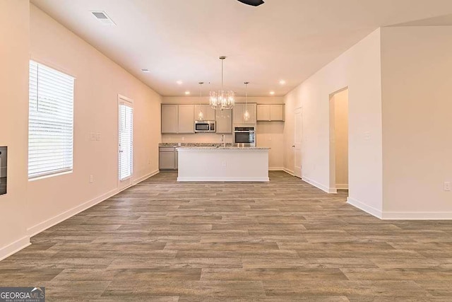 kitchen featuring decorative light fixtures, a chandelier, light hardwood / wood-style flooring, appliances with stainless steel finishes, and a kitchen island with sink