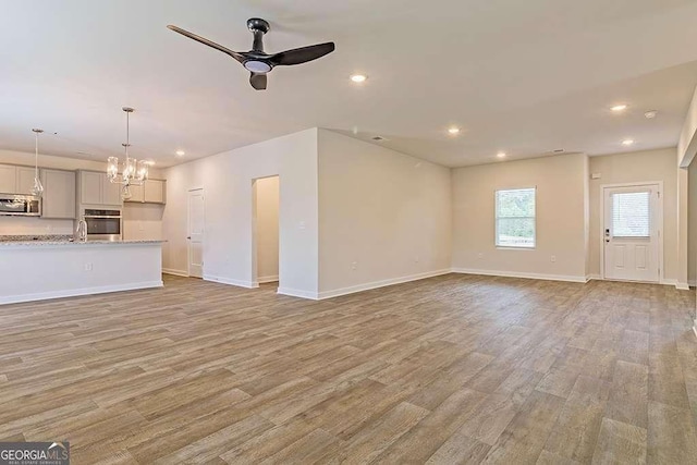 unfurnished living room with sink, ceiling fan with notable chandelier, and light hardwood / wood-style flooring