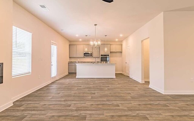 kitchen with a kitchen island with sink, pendant lighting, hardwood / wood-style flooring, and appliances with stainless steel finishes