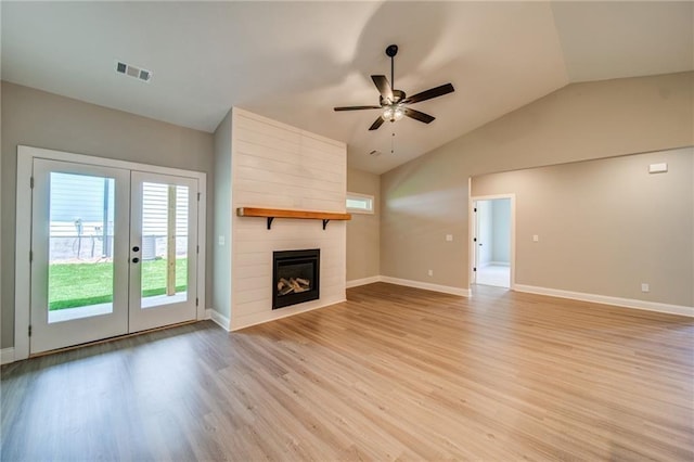 unfurnished living room featuring french doors, vaulted ceiling, a large fireplace, ceiling fan, and light hardwood / wood-style floors