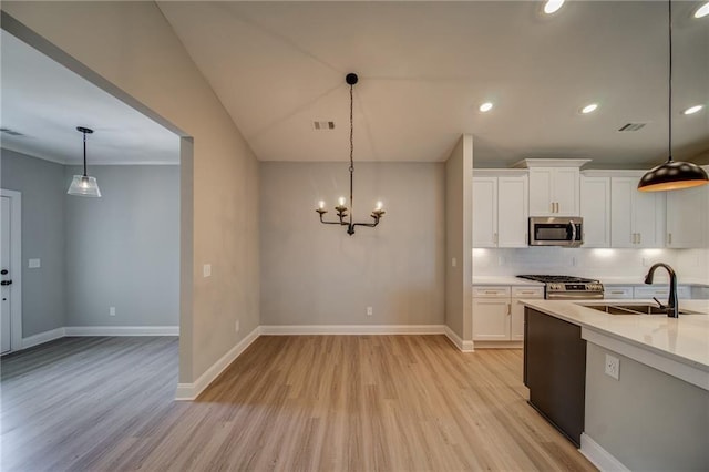 kitchen with sink, appliances with stainless steel finishes, white cabinetry, decorative light fixtures, and light wood-type flooring