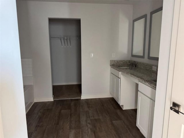 kitchen with baseboards, light stone counters, dark wood-style flooring, white cabinetry, and a sink