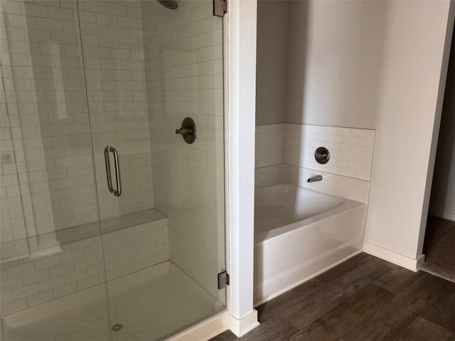 bathroom with a garden tub, a stall shower, wood finished floors, and baseboards