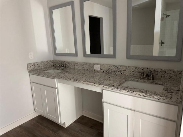 full bath featuring double vanity, a tile shower, a sink, and wood finished floors