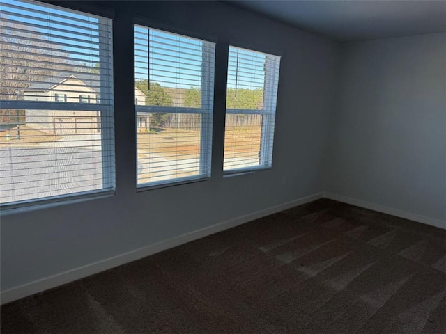 spare room featuring baseboards and dark carpet