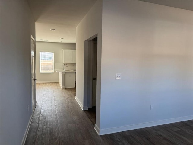 hallway featuring a sink, dark wood finished floors, and baseboards