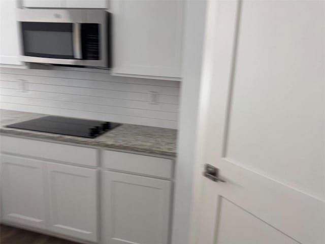 interior space with black electric stovetop, stainless steel microwave, white cabinets, and backsplash