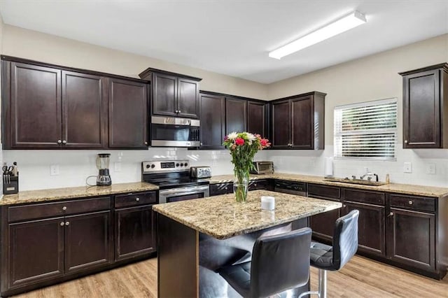 kitchen with a center island, stainless steel appliances, a breakfast bar area, dark brown cabinets, and light wood-type flooring