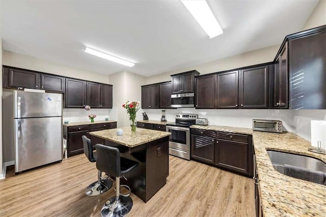 kitchen featuring stainless steel appliances, light stone counters, light hardwood / wood-style floors, dark brown cabinets, and a kitchen island