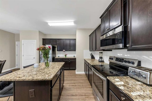 kitchen featuring light stone counters, a kitchen island, stainless steel appliances, and light hardwood / wood-style floors