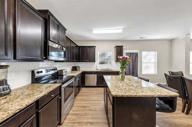 kitchen featuring sink, a kitchen island, appliances with stainless steel finishes, light hardwood / wood-style floors, and light stone counters