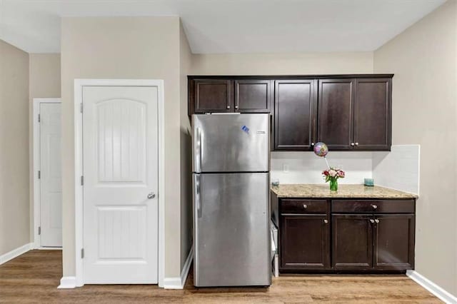 kitchen featuring stainless steel refrigerator, light stone counters, dark brown cabinetry, and light wood-type flooring