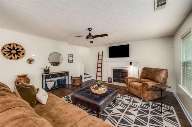 living area featuring a ceiling fan, a textured ceiling, a fireplace with flush hearth, and wood finished floors