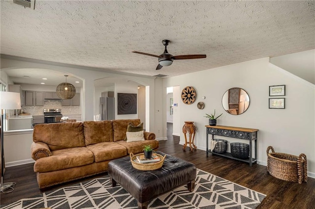 living room with ceiling fan, a textured ceiling, arched walkways, wood finished floors, and baseboards