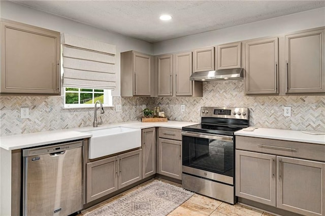 kitchen with a sink, light countertops, stainless steel appliances, backsplash, and under cabinet range hood