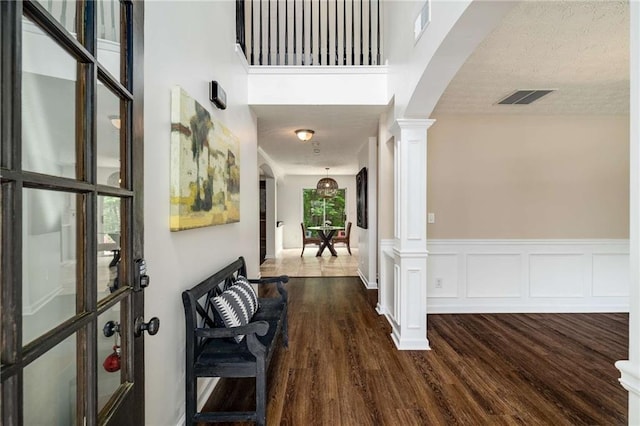 foyer entrance with arched walkways, decorative columns, dark wood finished floors, and visible vents