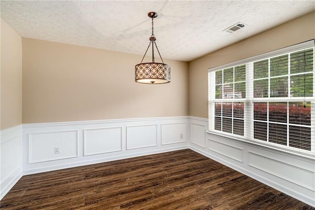 empty room with a decorative wall, dark wood finished floors, visible vents, and a wainscoted wall