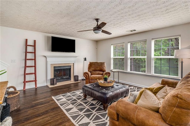 living room with visible vents, wood finished floors, a fireplace with raised hearth, a textured ceiling, and a ceiling fan
