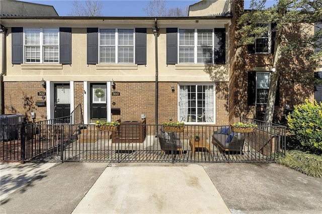 view of front of home featuring a fenced front yard, central AC, brick siding, a gate, and stucco siding