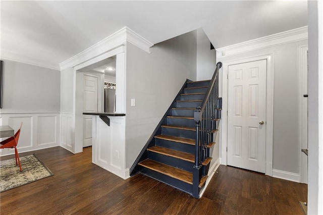 stairway with a wainscoted wall, crown molding, a decorative wall, and wood finished floors