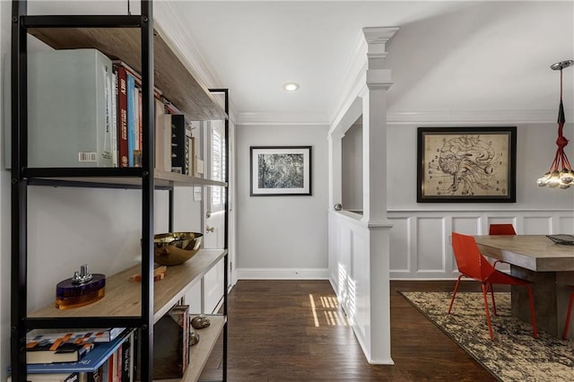 interior space featuring dark wood-style flooring, crown molding, ornate columns, a decorative wall, and baseboards