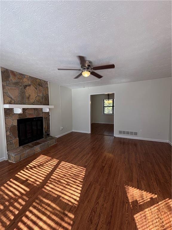 unfurnished living room with ceiling fan, a stone fireplace, dark hardwood / wood-style floors, and a textured ceiling