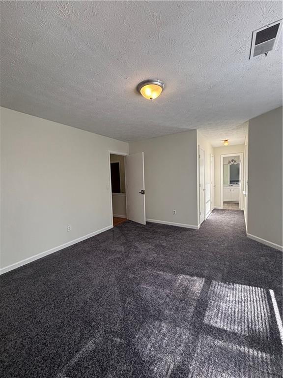 unfurnished room with a textured ceiling and dark colored carpet