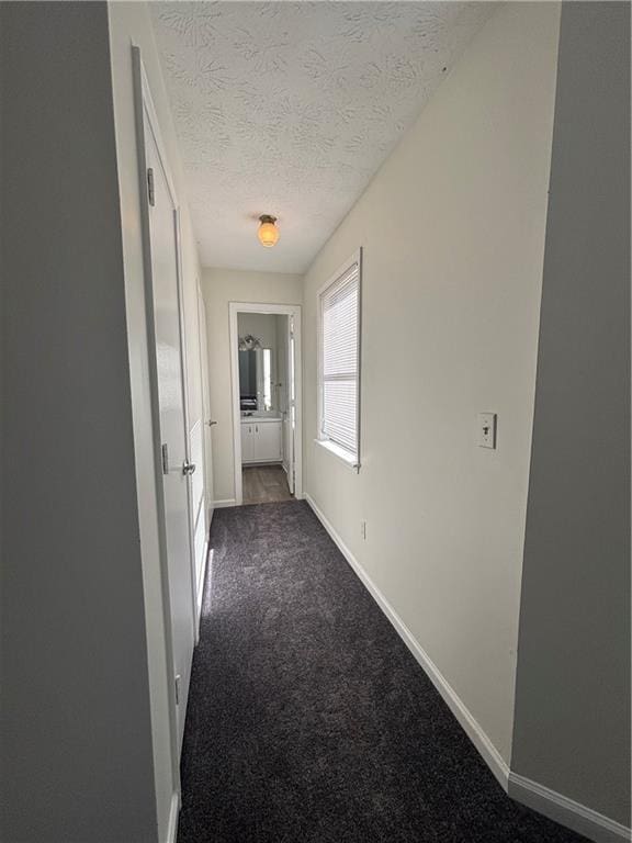 hall featuring dark carpet and a textured ceiling