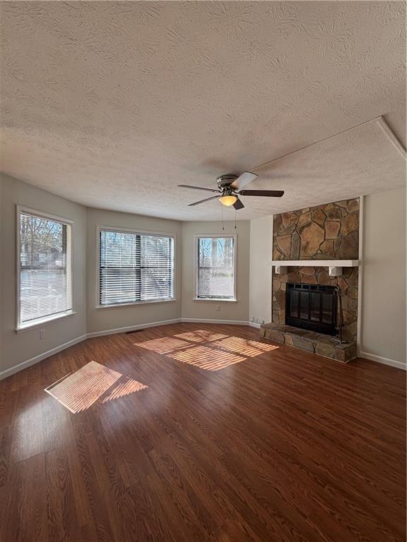 unfurnished living room featuring wood-type flooring, a stone fireplace, a wealth of natural light, and ceiling fan