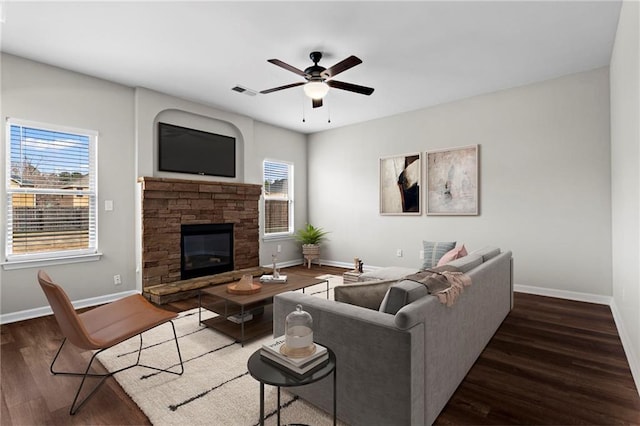 living room with baseboards, a stone fireplace, a ceiling fan, and wood finished floors