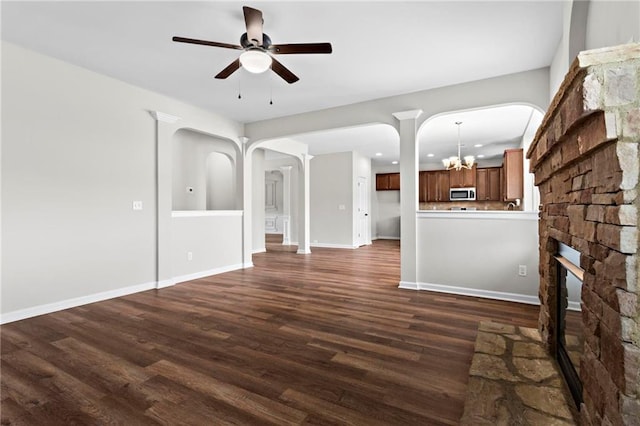 unfurnished living room featuring ceiling fan with notable chandelier, arched walkways, recessed lighting, baseboards, and dark wood-style floors