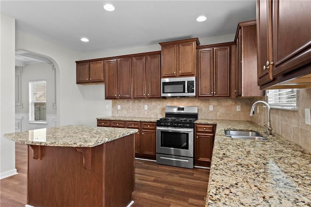 kitchen featuring arched walkways, a sink, dark wood finished floors, stainless steel appliances, and light stone counters