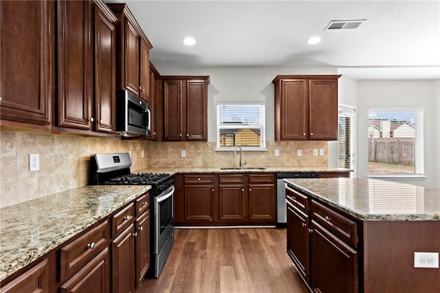 kitchen featuring dark wood-style floors, light stone countertops, visible vents, stainless steel appliances, and a sink