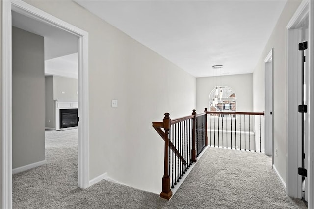hall with a chandelier, an upstairs landing, baseboards, and carpet floors
