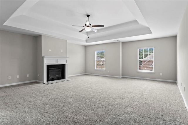 unfurnished living room featuring a healthy amount of sunlight, a tray ceiling, and ceiling fan