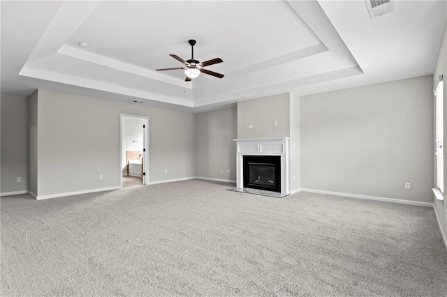 unfurnished living room with baseboards, a raised ceiling, visible vents, ceiling fan, and carpet