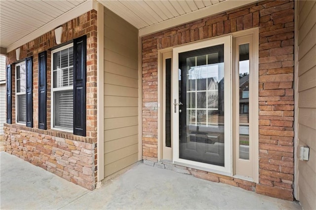 view of exterior entry with brick siding and covered porch