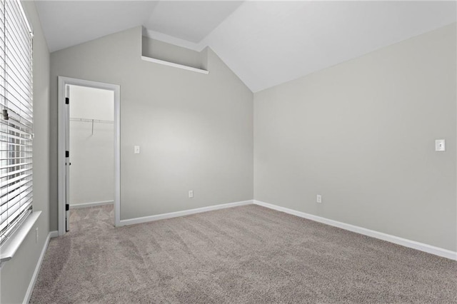 unfurnished bedroom featuring baseboards, a closet, a spacious closet, carpet flooring, and lofted ceiling