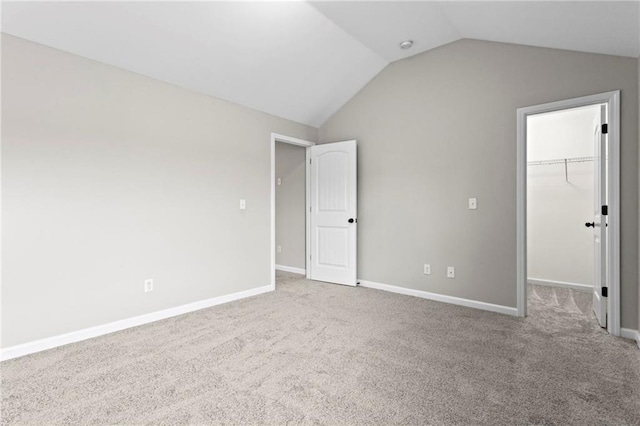 unfurnished bedroom featuring baseboards, vaulted ceiling, a closet, a spacious closet, and carpet