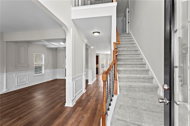 foyer featuring stairway, beam ceiling, coffered ceiling, a decorative wall, and wood finished floors