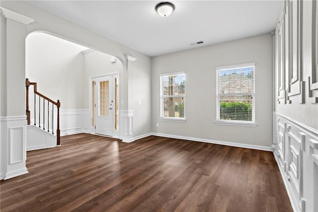 entrance foyer featuring dark wood-style flooring, stairway, visible vents, wainscoting, and a decorative wall