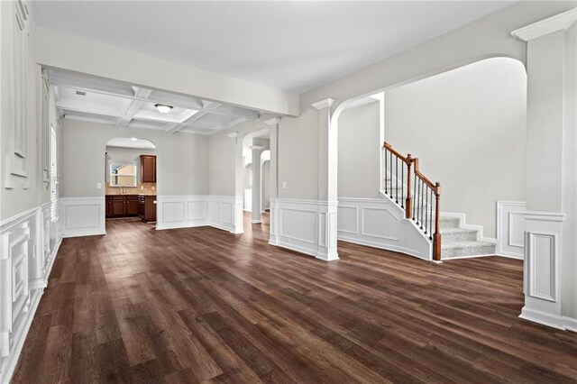unfurnished living room featuring decorative columns, beamed ceiling, dark wood finished floors, arched walkways, and coffered ceiling
