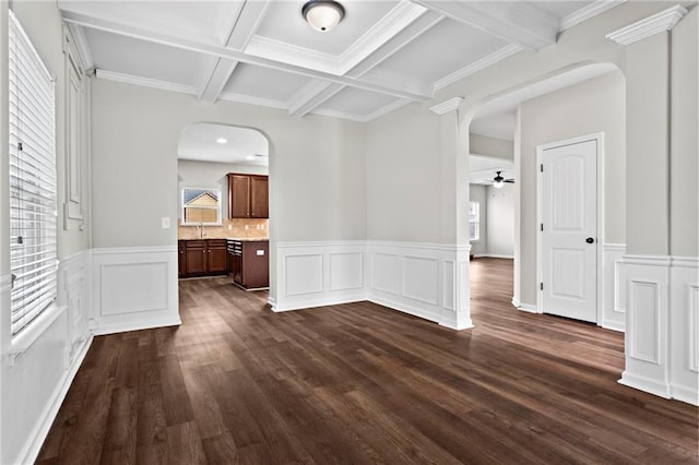 unfurnished dining area with arched walkways, a ceiling fan, dark wood finished floors, beamed ceiling, and coffered ceiling