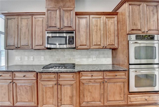 5195 Stefan Ridge Way, Buford, GA 30519 - kitchen with brown cabinetry, stainless steel appliances, backsplash, and dark stone counters