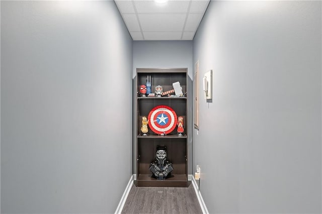 hall featuring a drop ceiling, wood finished floors, and baseboards