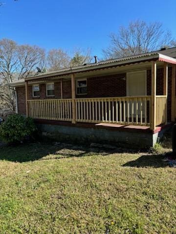 rear view of property with a lawn, covered porch, and brick siding