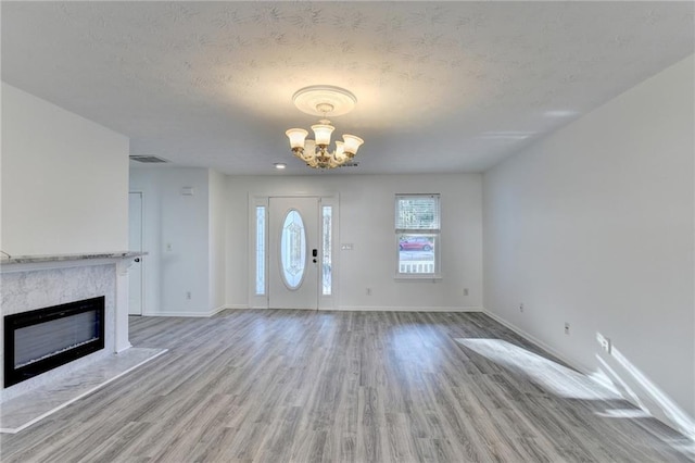 entryway with a notable chandelier, light hardwood / wood-style floors, and a textured ceiling