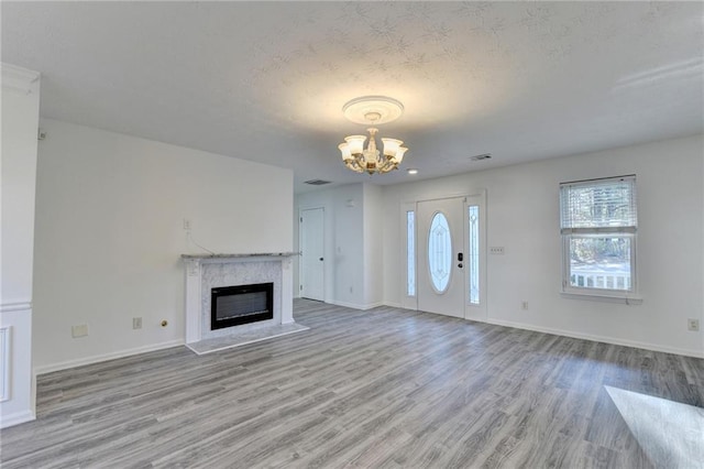 unfurnished living room featuring a textured ceiling, an inviting chandelier, light hardwood / wood-style flooring, and a premium fireplace