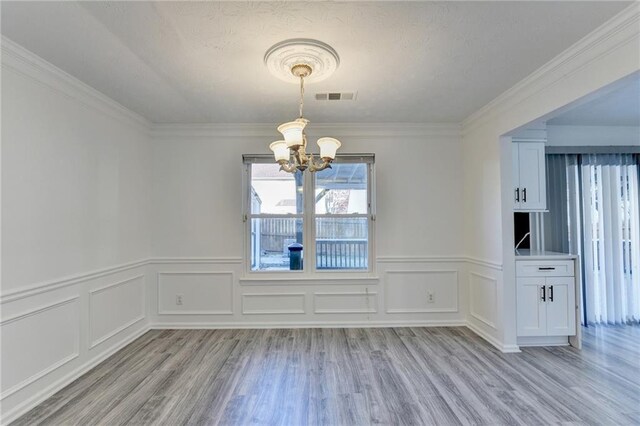 unfurnished dining area featuring light wood-type flooring, crown molding, and a chandelier